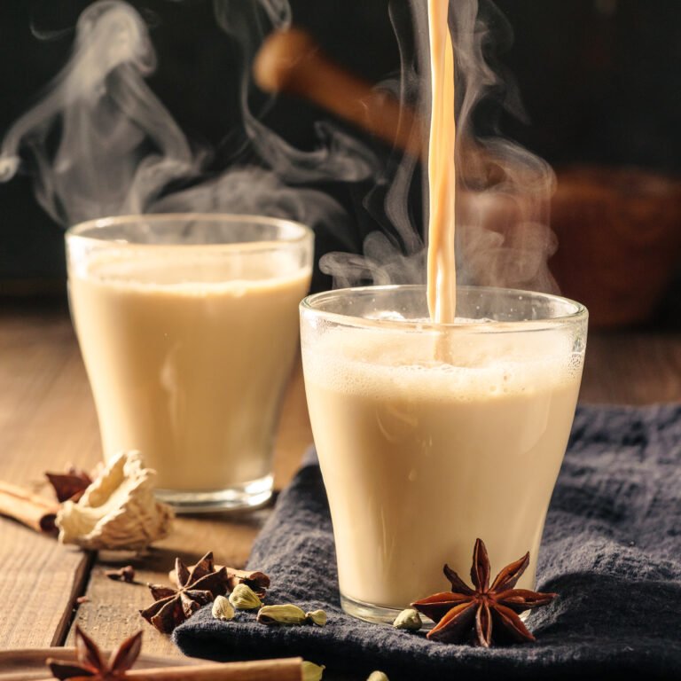 Masala tea with spices is poured into glass mugs on a wooden table.